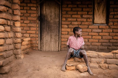 Boy smiling and sitting in front of a brick house
