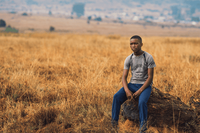 Senzo sits on a rock in a field thinking about how he needs a job.