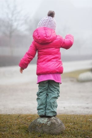 Little girl in pink coat standing on a rock